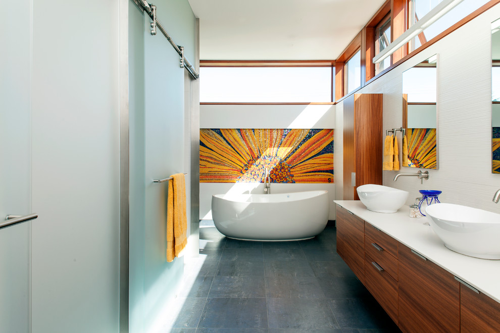Bild på ett stort funkis en-suite badrum, med ett fristående handfat, släta luckor, skåp i mellenmörkt trä, ett fristående badkar, en dusch i en alkov, grå kakel, bänkskiva i akrylsten, mosaik, vita väggar, klinkergolv i porslin och grått golv