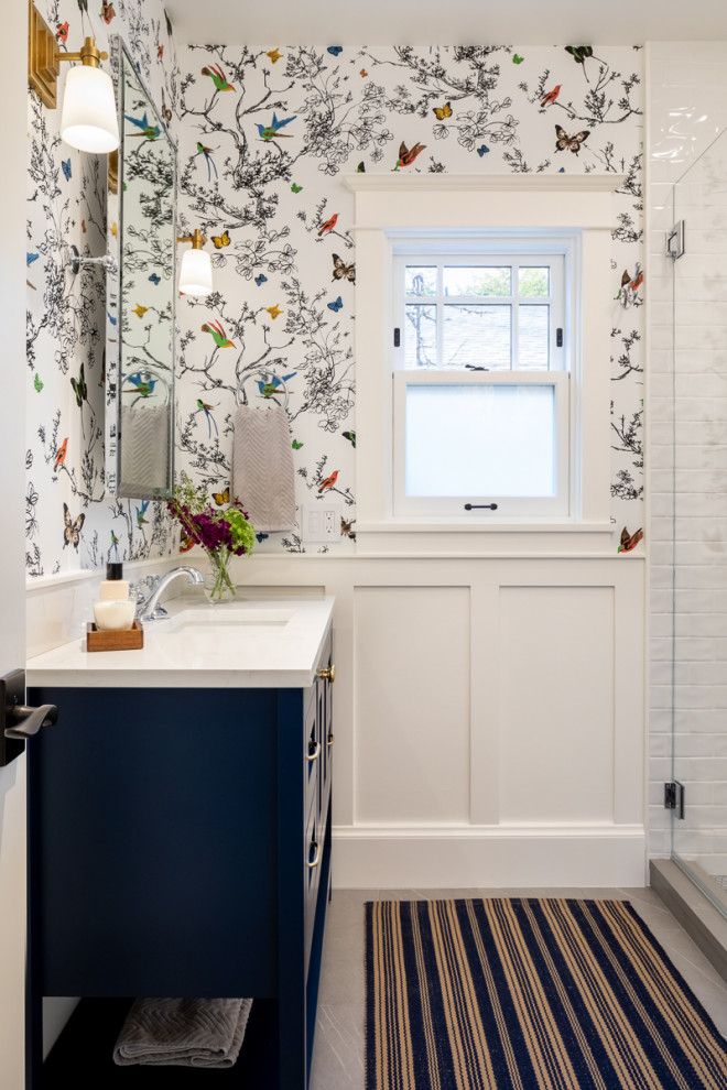 Пример оригинального дизайна: маленькая ванная комната в стиле неоклассика (современная классика) с фасадами островного типа, синими фасадами, унитазом-моноблоком, белой плиткой, керамогранитной плиткой, разноцветными стенами, полом из керамогранита, душевой кабиной, врезной раковиной, столешницей из искусственного кварца, серым полом, белой столешницей, нишей, тумбой под одну раковину, напольной тумбой и обоями на стенах для на участке и в саду