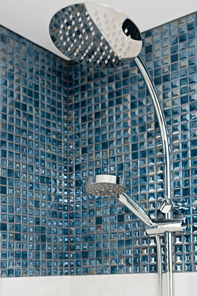 Inredning av ett klassiskt litet vit vitt badrum med dusch, med släta luckor, blå skåp, ett badkar i en alkov, en dusch/badkar-kombination, en toalettstol med hel cisternkåpa, blå kakel, mosaik, grå väggar, klinkergolv i porslin, bänkskiva i kvarts, dusch med gångjärnsdörr, ett undermonterad handfat och svart golv