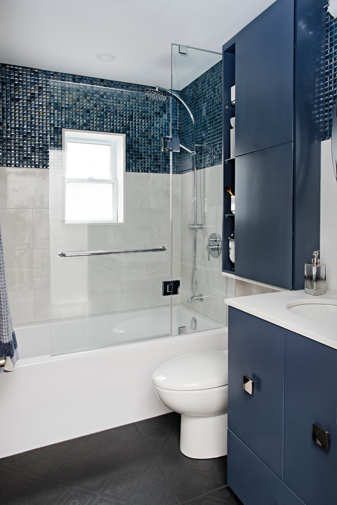 Klassisk inredning av ett litet vit vitt badrum med dusch, med släta luckor, blå skåp, ett badkar i en alkov, en dusch/badkar-kombination, en toalettstol med hel cisternkåpa, blå kakel, mosaik, grå väggar, klinkergolv i porslin, bänkskiva i kvarts, dusch med gångjärnsdörr, ett undermonterad handfat och svart golv