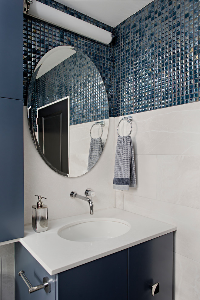 Inredning av ett klassiskt litet vit vitt badrum med dusch, med släta luckor, blå skåp, ett badkar i en alkov, en dusch/badkar-kombination, en toalettstol med hel cisternkåpa, blå kakel, mosaik, grå väggar, klinkergolv i porslin, bänkskiva i kvarts, dusch med gångjärnsdörr, ett undermonterad handfat och svart golv