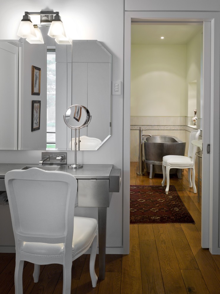 Cette image montre une salle de bain design avec un lavabo de ferme, un placard en trompe-l'oeil, un plan de toilette en acier inoxydable, une baignoire indépendante, une douche à l'italienne, WC séparés et un sol en bois brun.