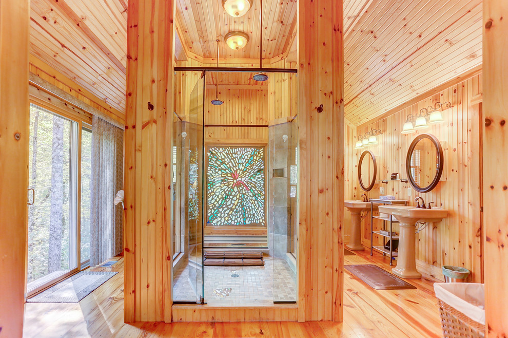 Cette image montre une salle de bain chalet avec une douche double, un mur marron, un sol en bois brun, un lavabo de ferme et une cabine de douche à porte battante.