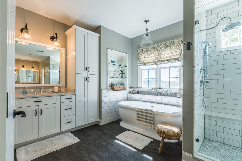 Inspiration for a large classic ensuite bathroom in DC Metro with shaker cabinets, white cabinets, a freestanding bath, an alcove shower, white tiles, metro tiles, grey walls, dark hardwood flooring, a submerged sink, engineered stone worktops, brown floors, a hinged door and grey worktops.
