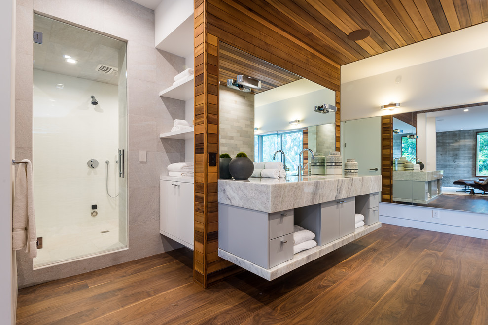 Foto på ett funkis vit en-suite badrum, med släta luckor, grå skåp, ett undermonterat badkar, en dusch i en alkov, grå kakel, vita väggar, mörkt trägolv, brunt golv och dusch med gångjärnsdörr