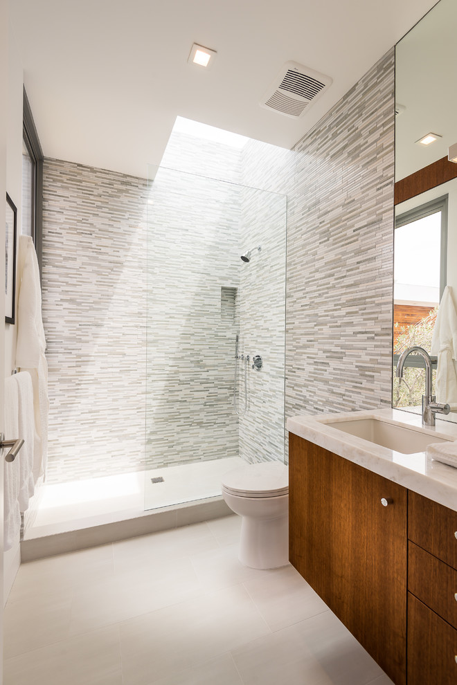Modernes Duschbad mit flächenbündigen Schrankfronten, dunklen Holzschränken, Duschnische, grauen Fliesen, Stäbchenfliesen, Unterbauwaschbecken, grauem Boden, offener Dusche und weißer Waschtischplatte in Los Angeles