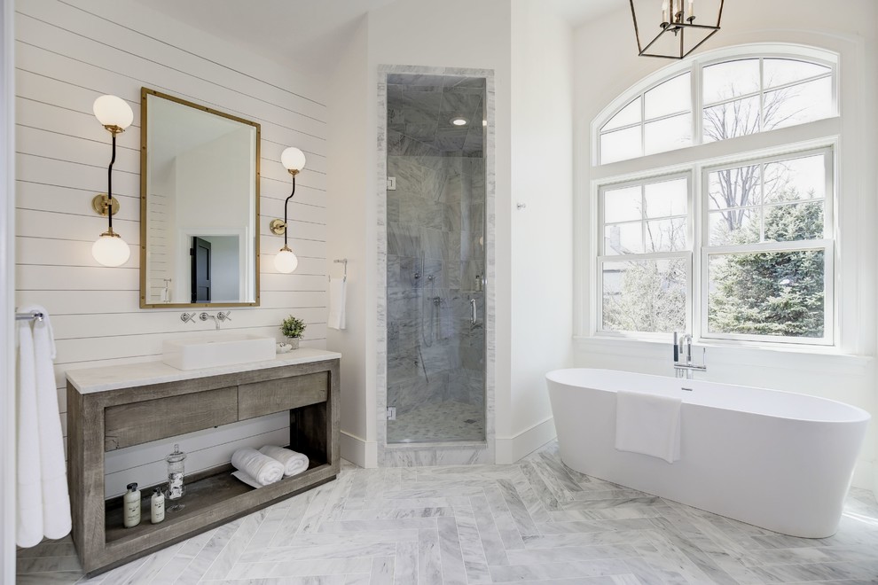На фото: ванная комната в стиле неоклассика (современная классика) с серыми фасадами, отдельно стоящей ванной, угловым душем, серой плиткой, белыми стенами, настольной раковиной, серым полом, белой столешницей и плоскими фасадами с