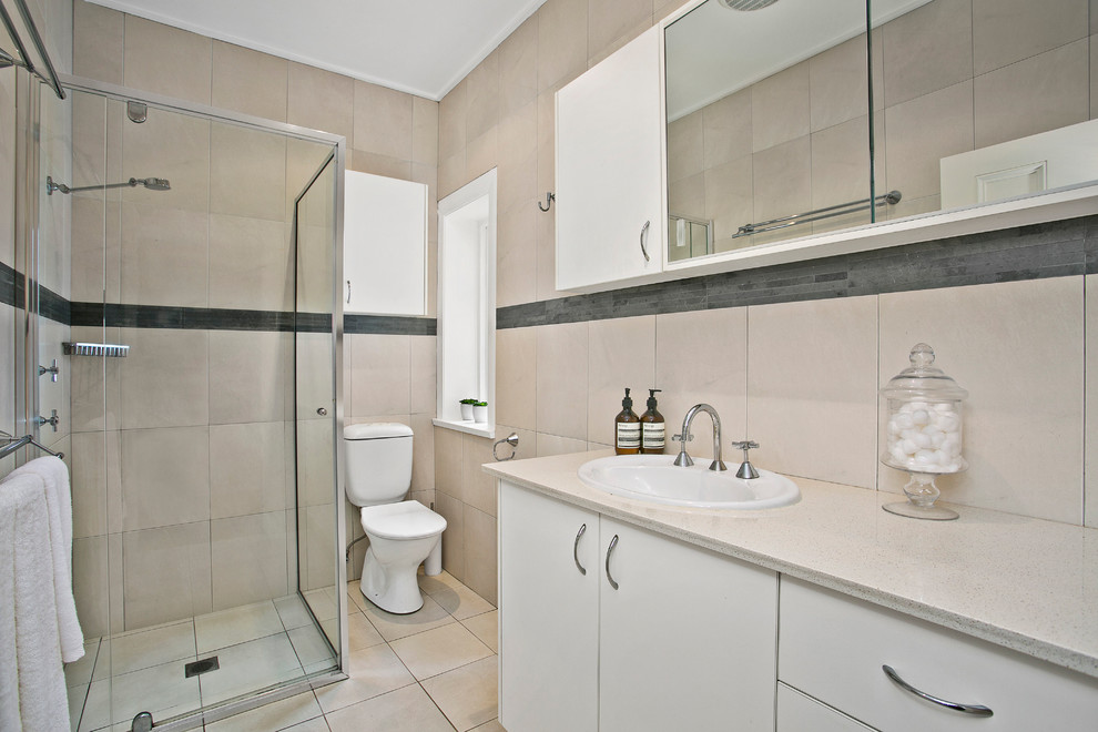 Exemple d'une petite salle de bain chic avec des portes de placard blanches, une douche d'angle, WC à poser, un carrelage beige, un carrelage de pierre, un mur beige, un lavabo posé et un plan de toilette en calcaire.