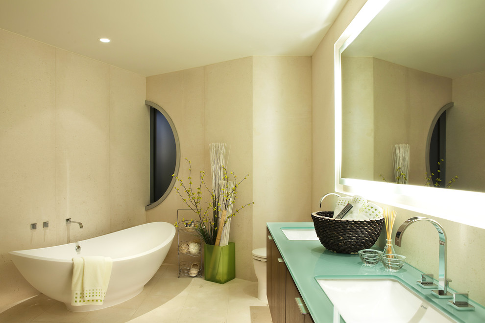На фото: ванная комната: освещение в современном стиле с отдельно стоящей ванной, стеклянной столешницей и бирюзовой столешницей с