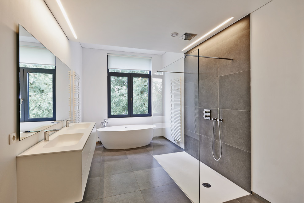 На фото: ванная комната в современном стиле с монолитной раковиной, плоскими фасадами, белыми фасадами, отдельно стоящей ванной, открытым душем, серой плиткой, белыми стенами и открытым душем