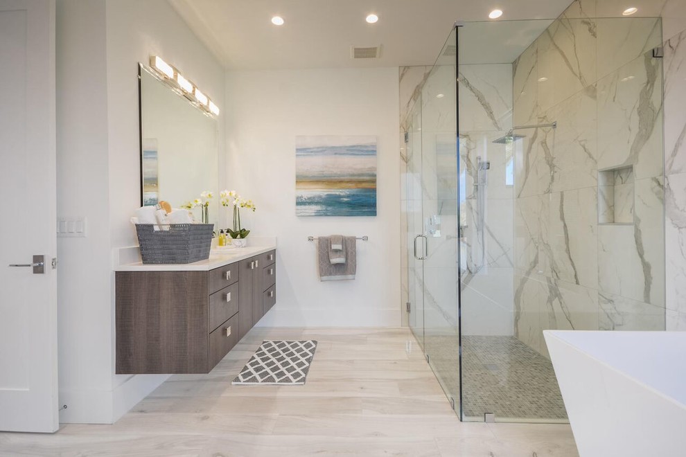 Inspiration for a contemporary ensuite bathroom in Miami with flat-panel cabinets, medium wood cabinets, a freestanding bath, a built-in shower, white tiles, white walls, marble flooring, solid surface worktops, white floors and a hinged door.