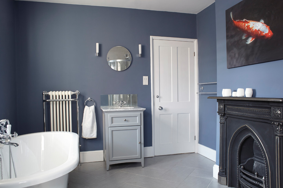 Foto di una stanza da bagno tradizionale di medie dimensioni con consolle stile comò, ante grigie, vasca con piedi a zampa di leone, pareti blu, lavabo sottopiano, top in marmo e pavimento grigio