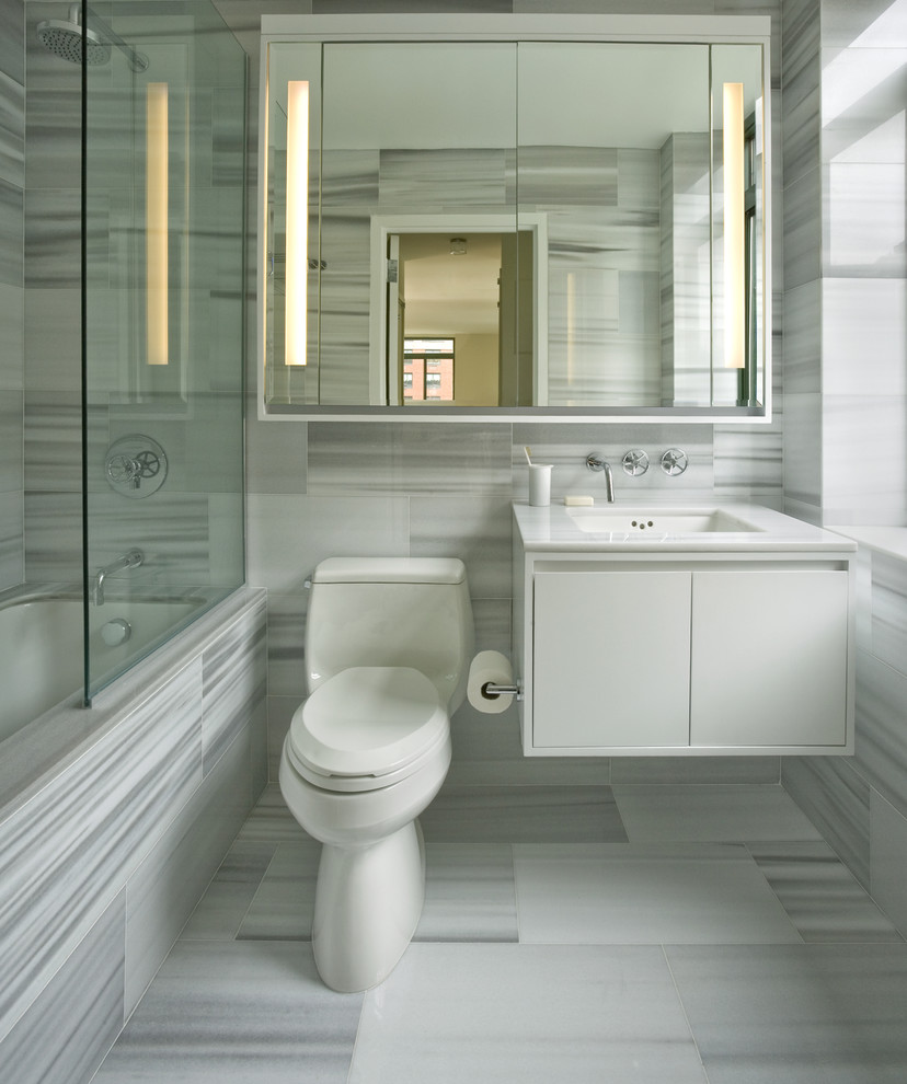 Cette image montre une salle de bain traditionnelle avec un lavabo encastré, un placard à porte plane, des portes de placard blanches, une baignoire encastrée, un combiné douche/baignoire et un carrelage gris.