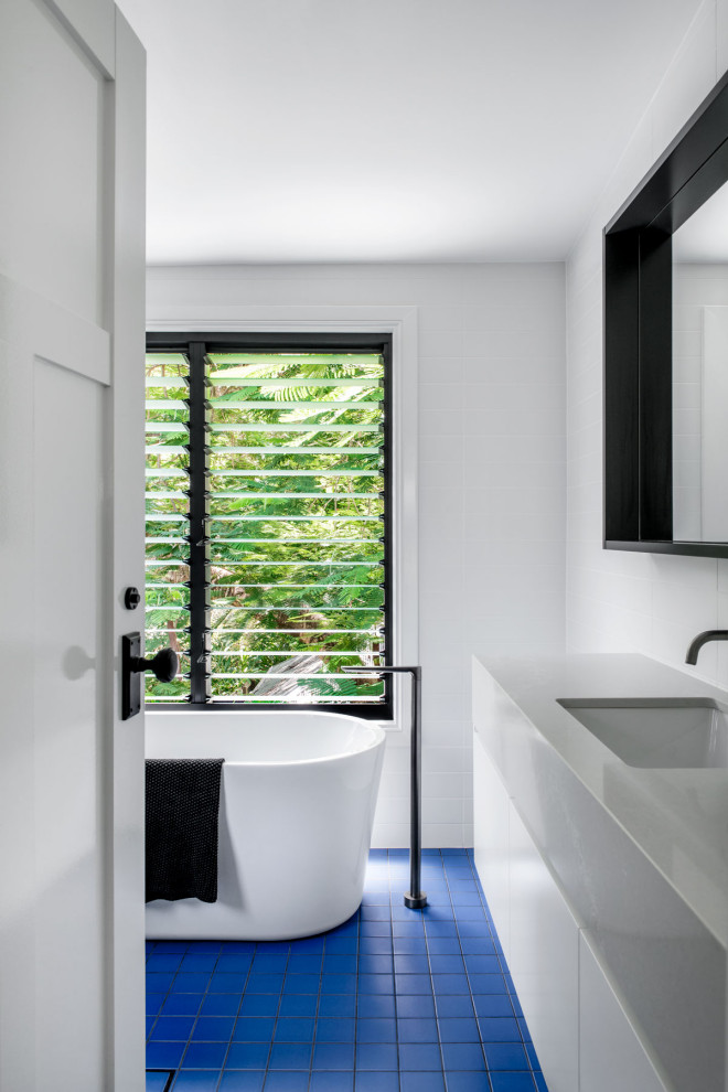 Idéer för mellanstora funkis grått en-suite badrum, med vita skåp, ett fristående badkar, vit kakel, vita väggar, bänkskiva i akrylsten, blått golv, släta luckor, klinkergolv i porslin och ett undermonterad handfat
