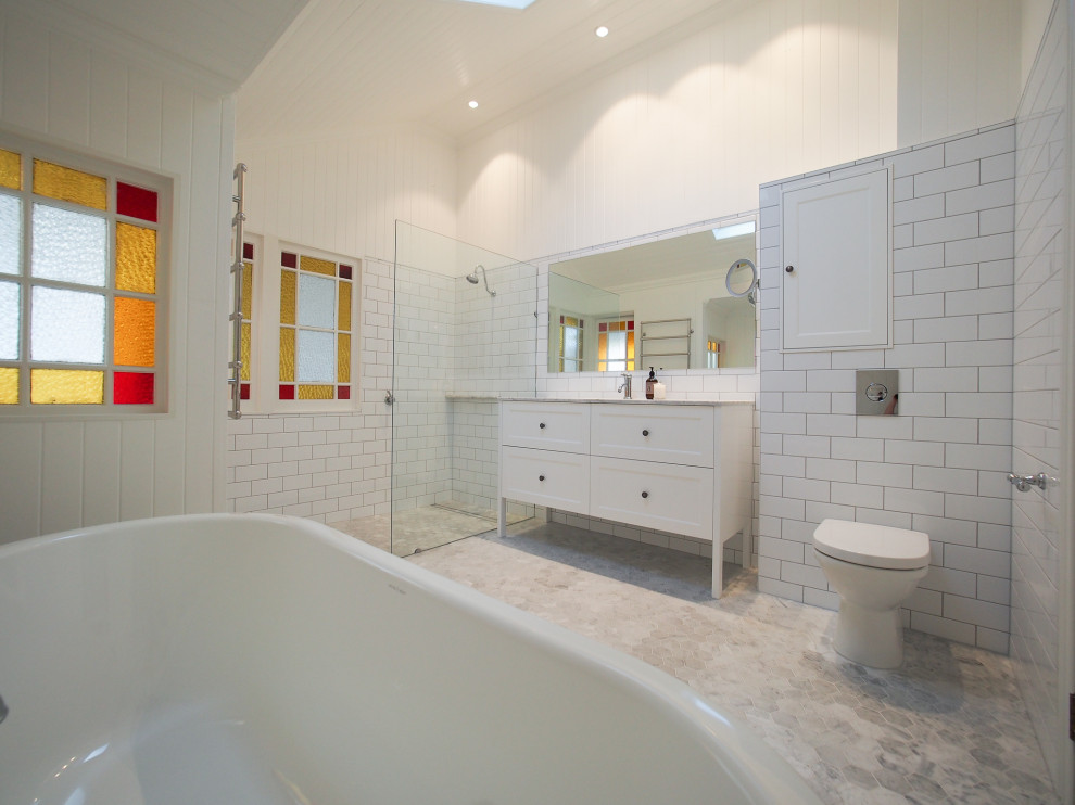 Large classic ensuite bathroom with beaded cabinets, white cabinets, a freestanding bath, a built-in shower, a one-piece toilet, white tiles, porcelain tiles, white walls, marble flooring, a submerged sink and marble worktops.