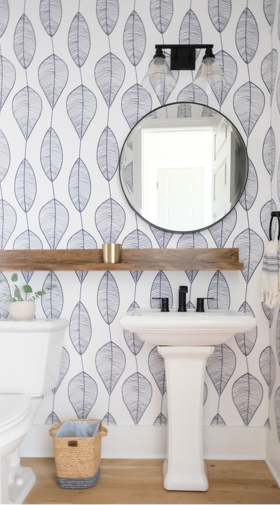This is an example of a small coastal shower room bathroom in Charleston with a one-piece toilet, blue tiles, light hardwood flooring, a pedestal sink, a single sink and wallpapered walls.