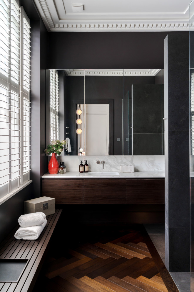 Modernes Badezimmer mit flächenbündigen Schrankfronten, dunklen Holzschränken, schwarzer Wandfarbe, dunklem Holzboden, Unterbauwaschbecken, braunem Boden, weißer Waschtischplatte, Einzelwaschbecken und schwebendem Waschtisch in London