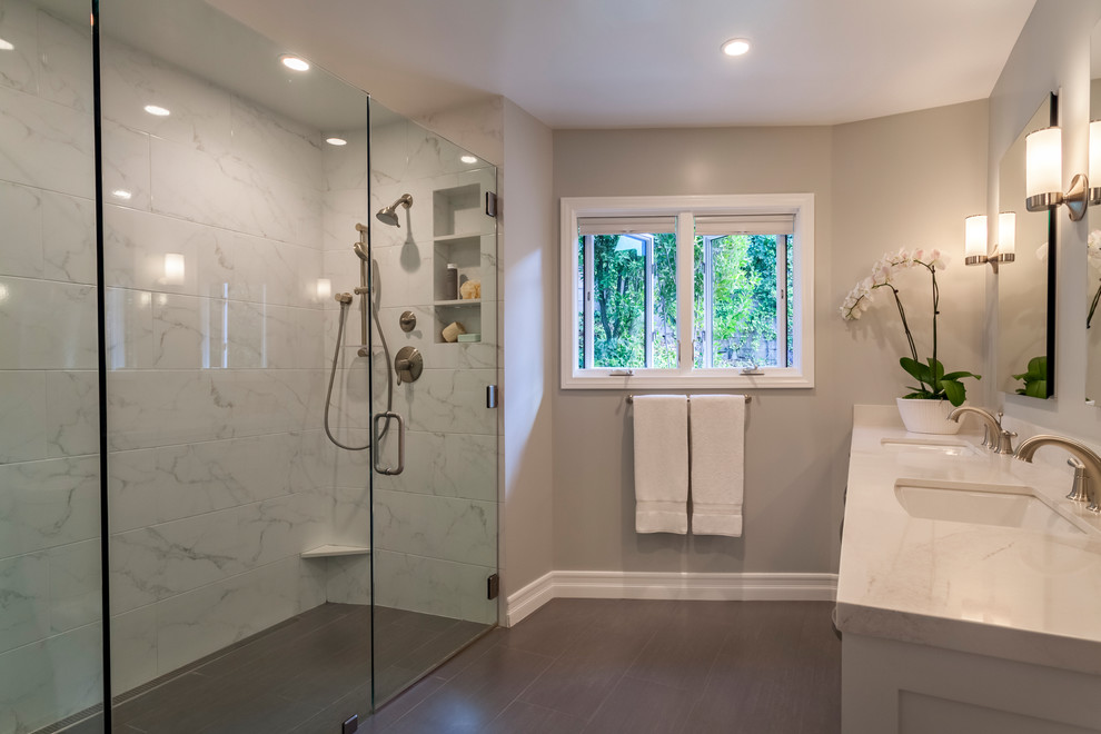 Inspiration for a large transitional 3/4 white tile and porcelain tile brown floor walk-in shower remodel in Los Angeles with shaker cabinets, white cabinets, a wall-mount toilet, beige walls, an undermount sink, quartz countertops and a hinged shower door