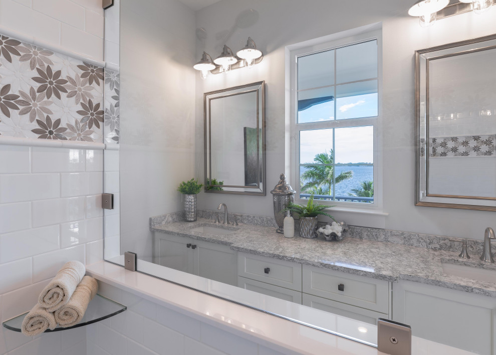 Photo of a large coastal ensuite bathroom in Tampa with shaker cabinets, white cabinets, a freestanding bath, a double shower, a two-piece toilet, multi-coloured tiles, mosaic tiles, grey walls, mosaic tile flooring, a submerged sink, granite worktops, multi-coloured floors, grey worktops, an enclosed toilet, double sinks and a vaulted ceiling.