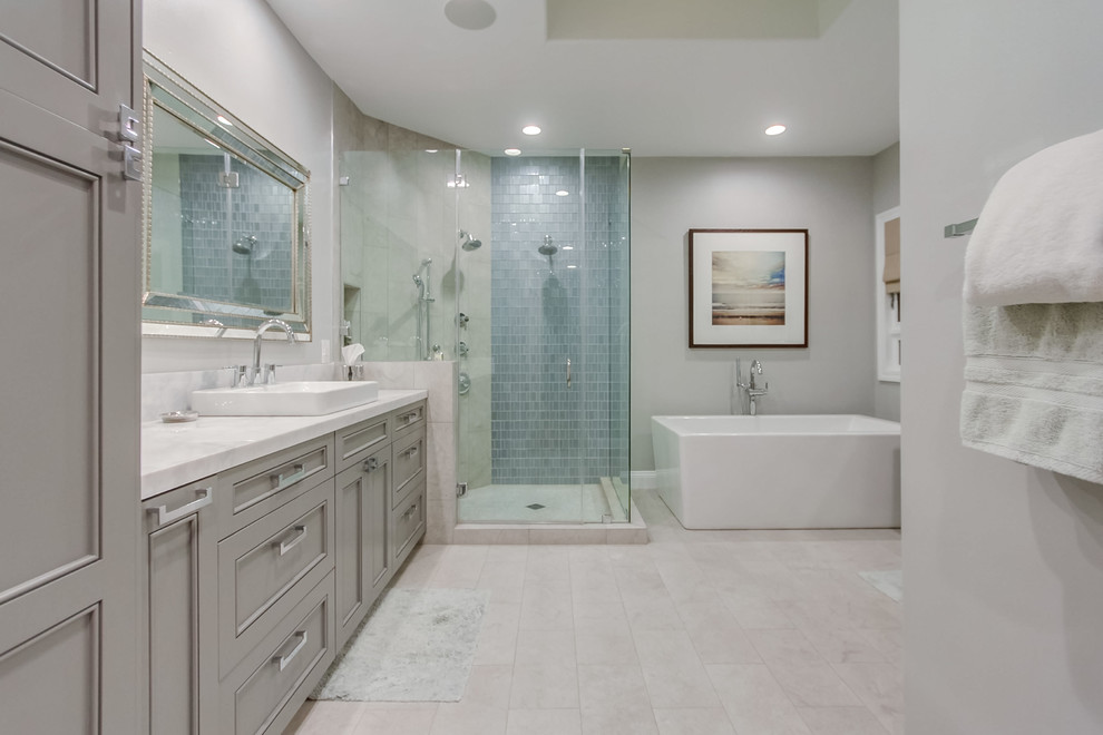 Cette image montre une grande salle de bain principale design avec un placard avec porte à panneau encastré, des portes de placard grises, une baignoire indépendante, une douche d'angle, un mur gris, un sol en marbre, une vasque et un plan de toilette en marbre.