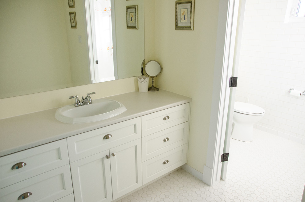 Klassisk inredning av ett mellanstort badrum, med ett nedsänkt handfat, skåp i shakerstil, vita skåp, laminatbänkskiva, vit kakel, keramikplattor, gula väggar och klinkergolv i keramik