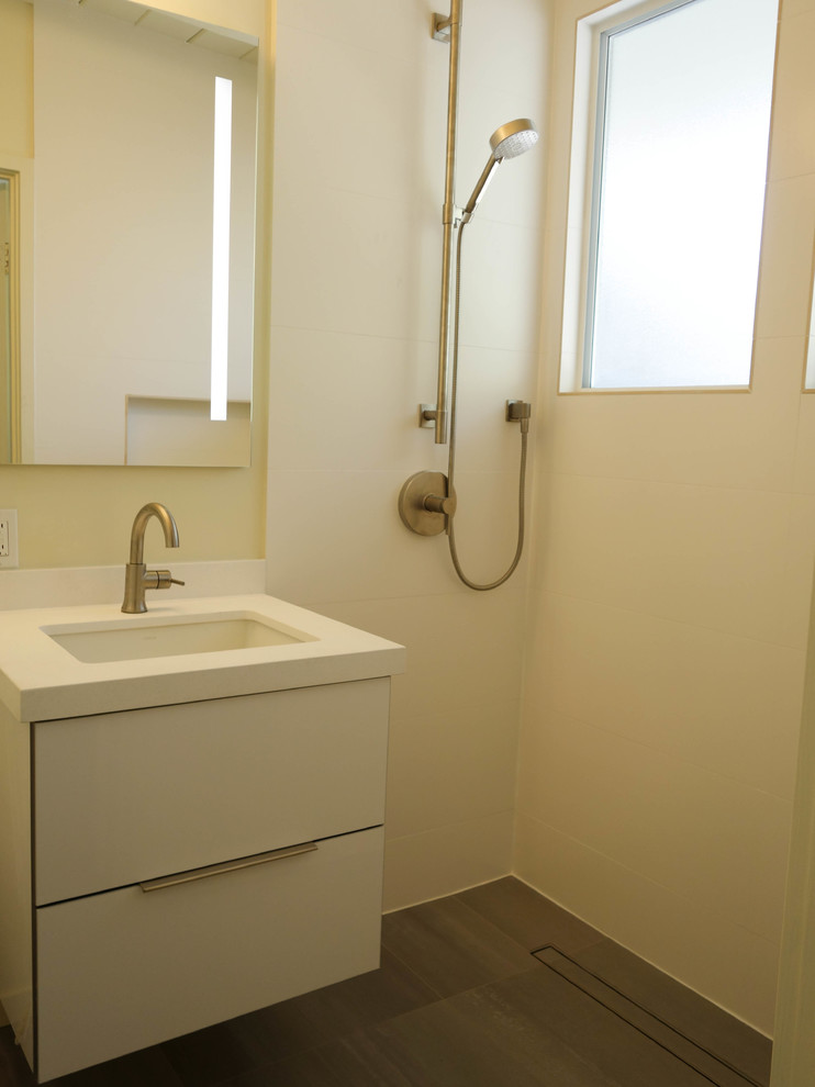 Retro inredning av ett mellanstort vit vitt badrum med dusch, med släta luckor, vita skåp, en dusch i en alkov, en toalettstol med separat cisternkåpa, vit kakel, porslinskakel, vita väggar, betonggolv, ett undermonterad handfat, bänkskiva i kvarts, grått golv och dusch med gångjärnsdörr