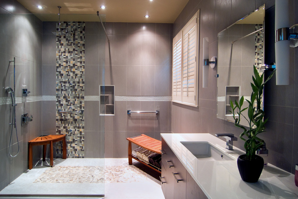 Modern ensuite bathroom in Oklahoma City with a submerged sink, flat-panel cabinets, dark wood cabinets, solid surface worktops, a walk-in shower, a one-piece toilet, grey tiles, beige walls, ceramic flooring and glass tiles.
