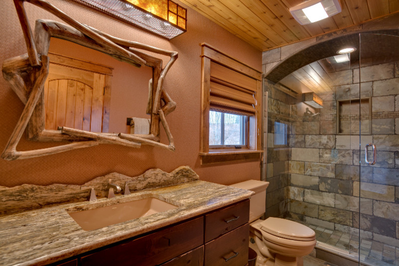 Design ideas for a medium sized rustic shower room bathroom in Other with flat-panel cabinets, medium wood cabinets, an alcove shower, a two-piece toilet, grey tiles, stone tiles, brown walls, porcelain flooring, a submerged sink, granite worktops and a hinged door.
