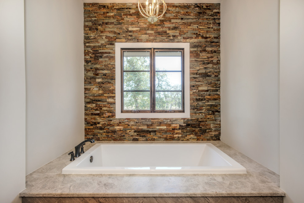 Immagine di una stanza da bagno rustica con vasca da incasso, piastrelle bianche, lastra di pietra, pavimento in cemento, top in marmo e pavimento marrone