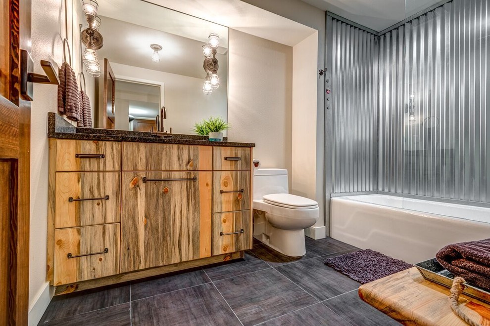 Cette photo montre une salle de bain montagne en bois brun de taille moyenne avec un placard à porte plane, une baignoire en alcôve, un combiné douche/baignoire, WC à poser, un carrelage gris, carrelage en métal, un mur beige, un sol en carrelage de porcelaine, un lavabo encastré et un plan de toilette en granite.