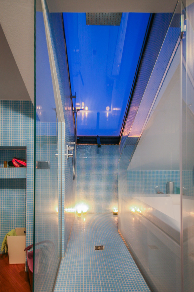 Ispirazione per una stanza da bagno padronale minimal con lavabo sospeso, ante blu, doccia aperta, WC a due pezzi, piastrelle blu, piastrelle a mosaico, pareti blu, pavimento in legno massello medio e vasca idromassaggio