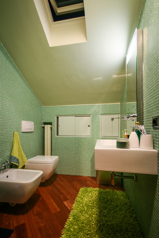 Modernes Duschbad mit Wandwaschbecken, blauen Schränken, Wandtoilette mit Spülkasten, grünen Fliesen, Mosaikfliesen, grüner Wandfarbe und braunem Holzboden in Mailand