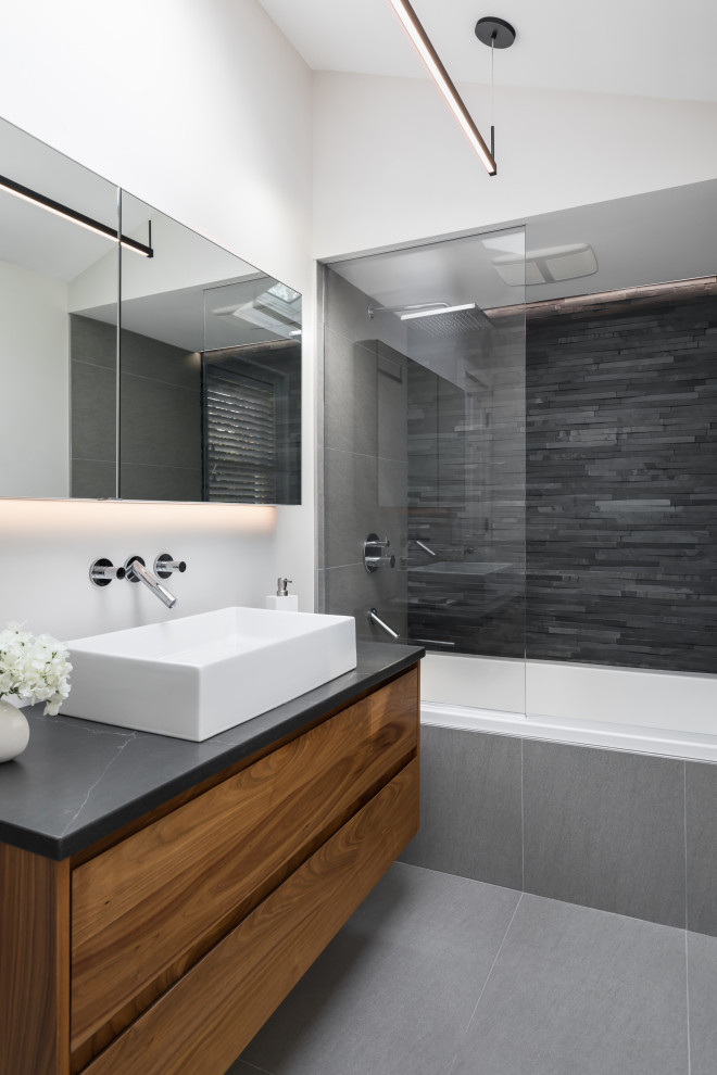 Inspiration pour une petite salle de bain principale minimaliste en bois brun avec un placard à porte plane, une baignoire en alcôve, un carrelage gris, une vasque, un plan de toilette en quartz modifié, un sol gris, aucune cabine et un plan de toilette noir.