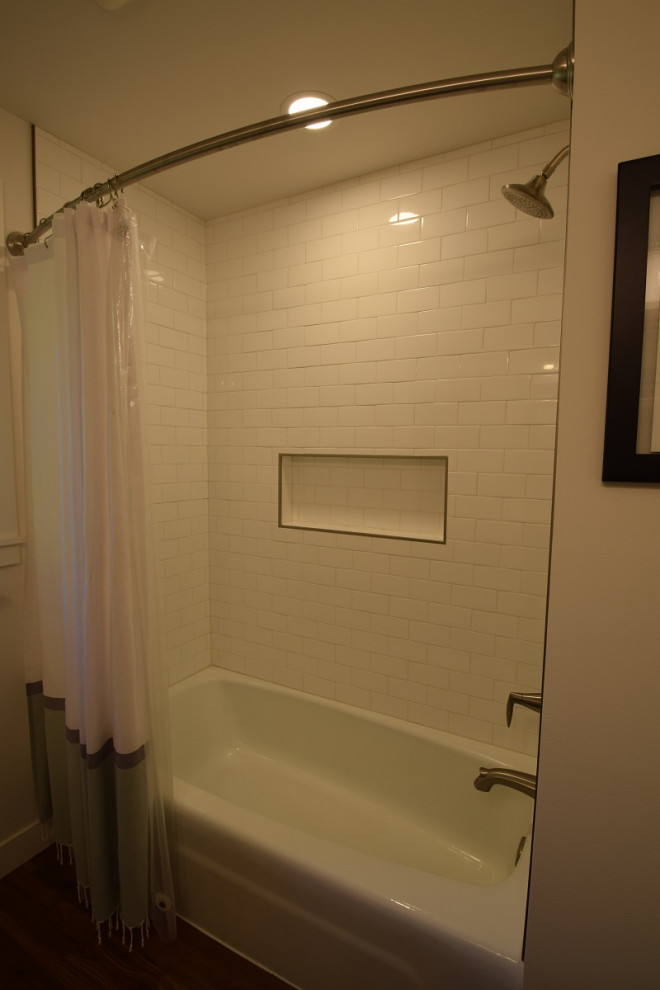 Inredning av ett klassiskt mellanstort vit vitt badrum, med skåp i shakerstil, blå skåp, ett badkar i en alkov, en dusch i en alkov, en toalettstol med hel cisternkåpa, vit kakel, tunnelbanekakel, vita väggar, mellanmörkt trägolv, ett undermonterad handfat, bänkskiva i kvarts och dusch med duschdraperi