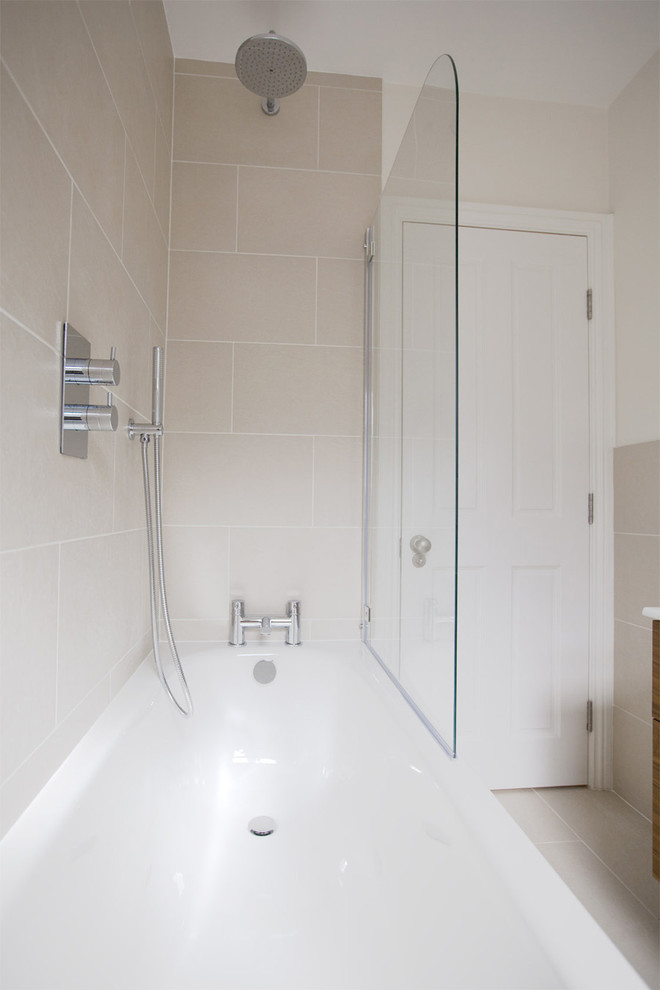 This is an example of a medium sized contemporary family bathroom in London with flat-panel cabinets, dark wood cabinets, a built-in bath, a shower/bath combination, a two-piece toilet, grey tiles, ceramic tiles, grey walls, ceramic flooring and an integrated sink.