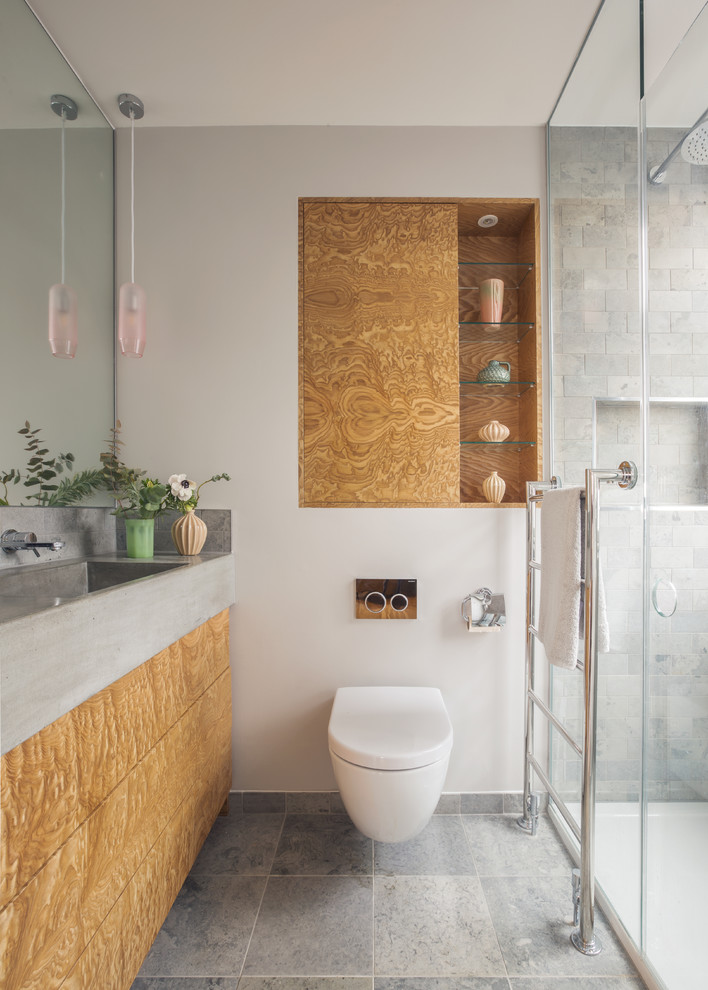 Inredning av ett modernt grå grått badrum med dusch, med släta luckor, bruna skåp, en dusch i en alkov, en vägghängd toalettstol, grå kakel, tunnelbanekakel, vita väggar, ett integrerad handfat, bänkskiva i betong och grått golv