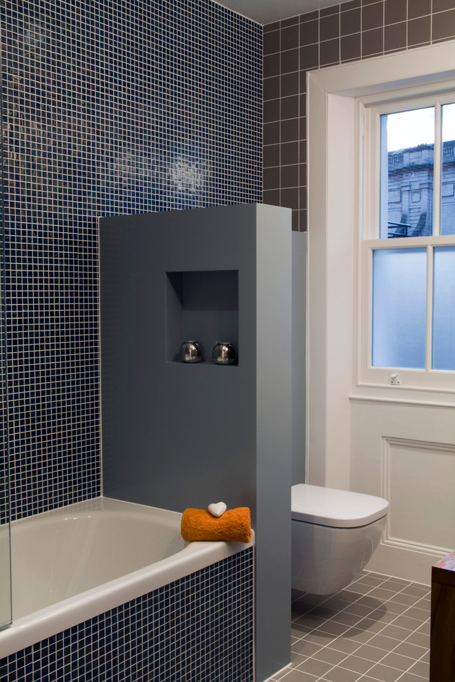Design ideas for a small modern ensuite bathroom in London with a vessel sink, a built-in bath, a shower/bath combination, a wall mounted toilet, blue tiles, glass tiles, grey walls and ceramic flooring.