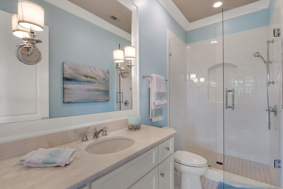 Example of a mid-sized beach style 3/4 beige tile, white tile and stone slab ceramic tile alcove shower design in Miami with recessed-panel cabinets, white cabinets, a two-piece toilet, blue walls, an undermount sink and solid surface countertops