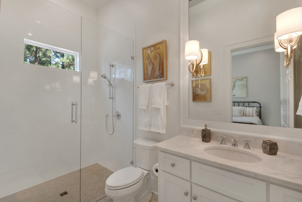Foto på ett mellanstort maritimt badrum med dusch, med luckor med infälld panel, vita skåp, en dusch i en alkov, en toalettstol med separat cisternkåpa, grå kakel, vit kakel, stenhäll, vita väggar, ett undermonterad handfat och bänkskiva i akrylsten
