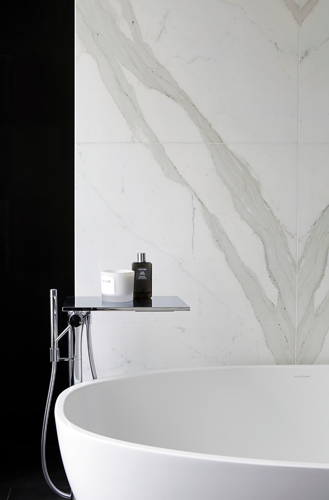 Ejemplo de cuarto de baño principal, actual, de tamaño medio, con armarios con paneles lisos, puertas de armario marrones, bañera exenta, ducha abierta, sanitario de pared, baldosas y/o azulejos blancas y negros, baldosas y/o azulejos de mármol, paredes grises, suelo de mármol, lavabo suspendido y encimera de mármol