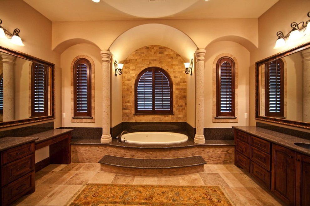 This is an example of a medium sized mediterranean ensuite bathroom in Austin with raised-panel cabinets, dark wood cabinets, an alcove bath, beige tiles, stone tiles, beige walls, a submerged sink, granite worktops, porcelain flooring and beige floors.