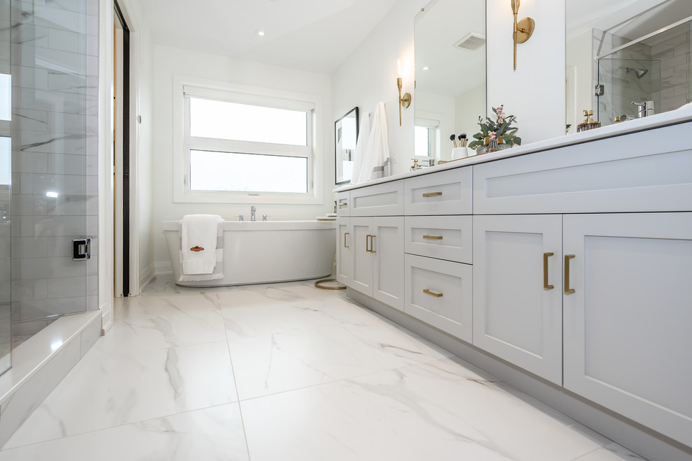Cette image montre une grande salle de bain principale minimaliste avec des portes de placard blanches, une baignoire indépendante, un carrelage blanc, des carreaux de porcelaine, un mur blanc, un sol en carrelage de porcelaine, un sol blanc et un plan de toilette blanc.