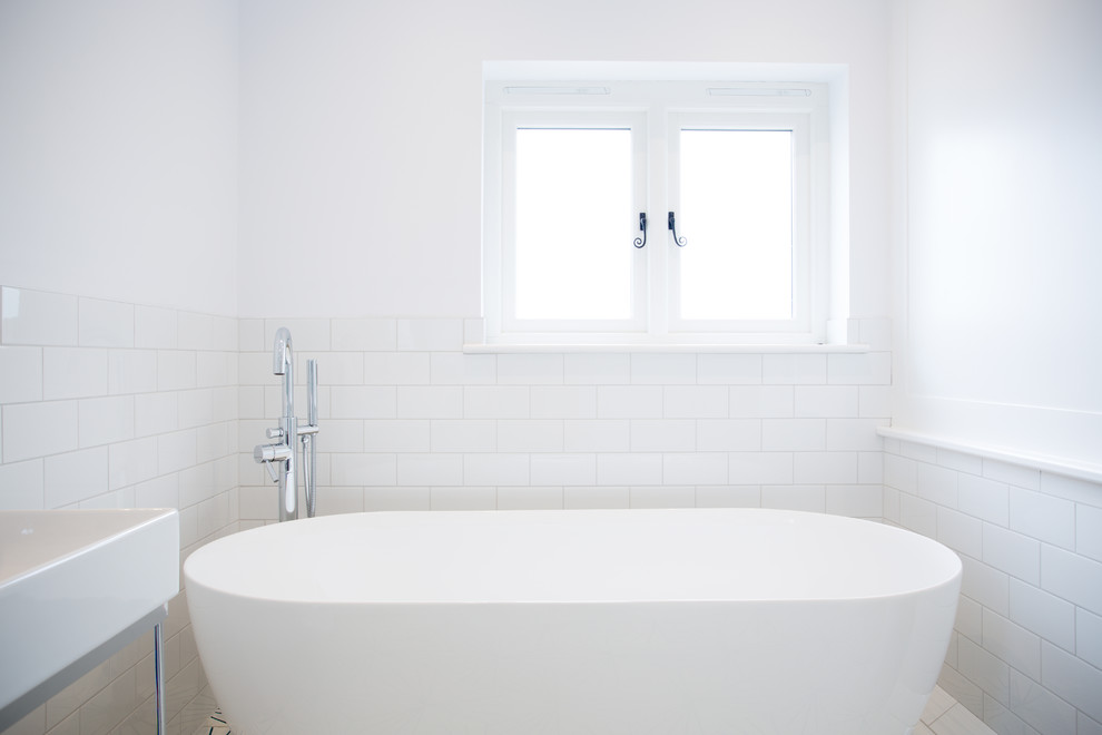 Foto på ett litet funkis badrum för barn, med möbel-liknande, vita skåp, ett fristående badkar, vit kakel, tunnelbanekakel och ett konsol handfat