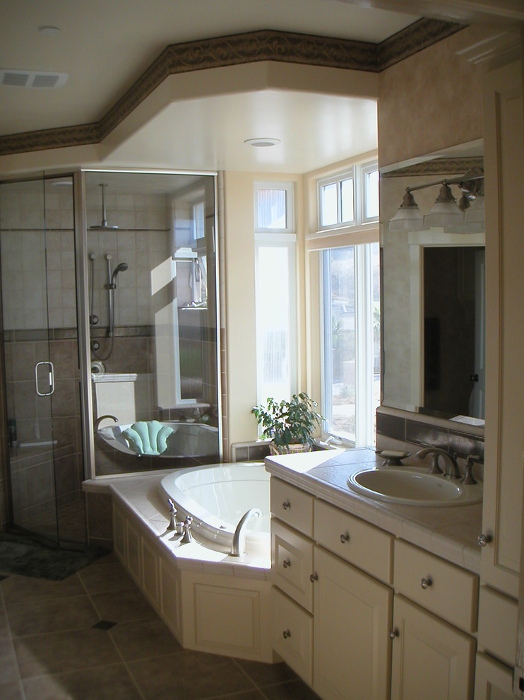 На фото: большая главная ванная комната в стиле кантри с фасадами в стиле шейкер, белыми фасадами, накладной ванной, угловым душем, разноцветной плиткой, керамогранитной плиткой, столешницей из плитки, душем с распашными дверями, белой столешницей, тумбой под одну раковину, встроенной тумбой, унитазом-моноблоком, бежевыми стенами, полом из керамической плитки, накладной раковиной, разноцветным полом и многоуровневым потолком