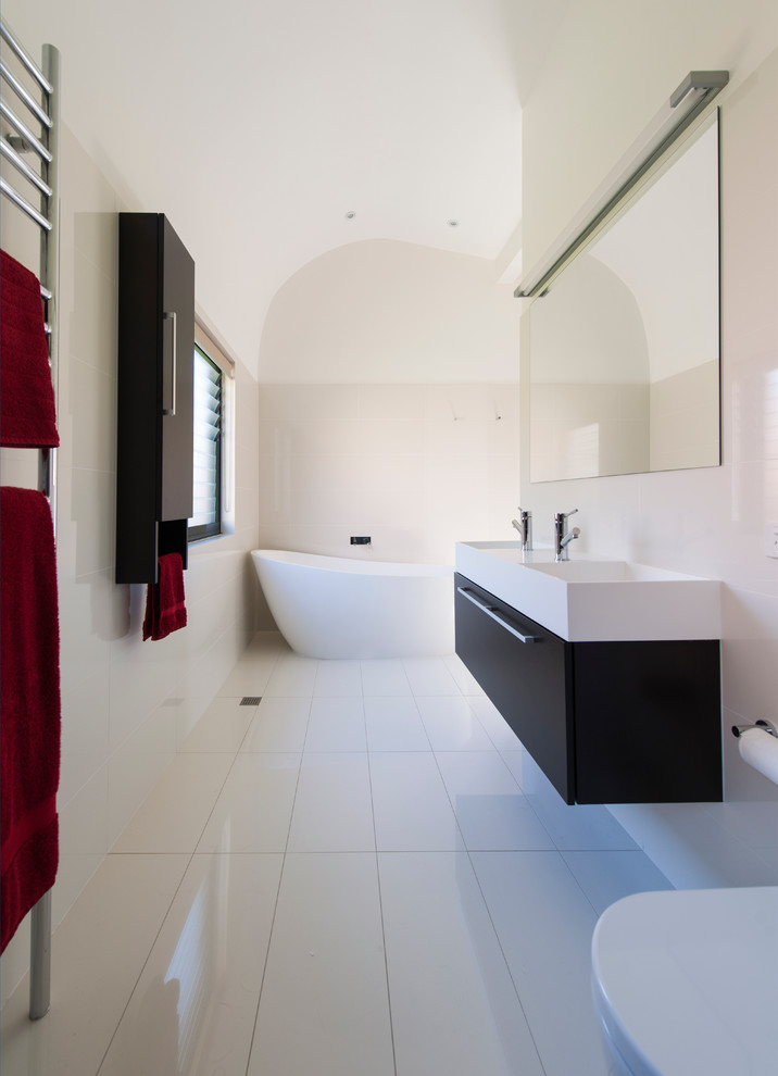 Exempel på ett stort modernt en-suite badrum, med ett integrerad handfat, svarta skåp, ett fristående badkar, en dubbeldusch, en toalettstol med hel cisternkåpa, vit kakel, porslinskakel, vita väggar, klinkergolv i keramik och vitt golv