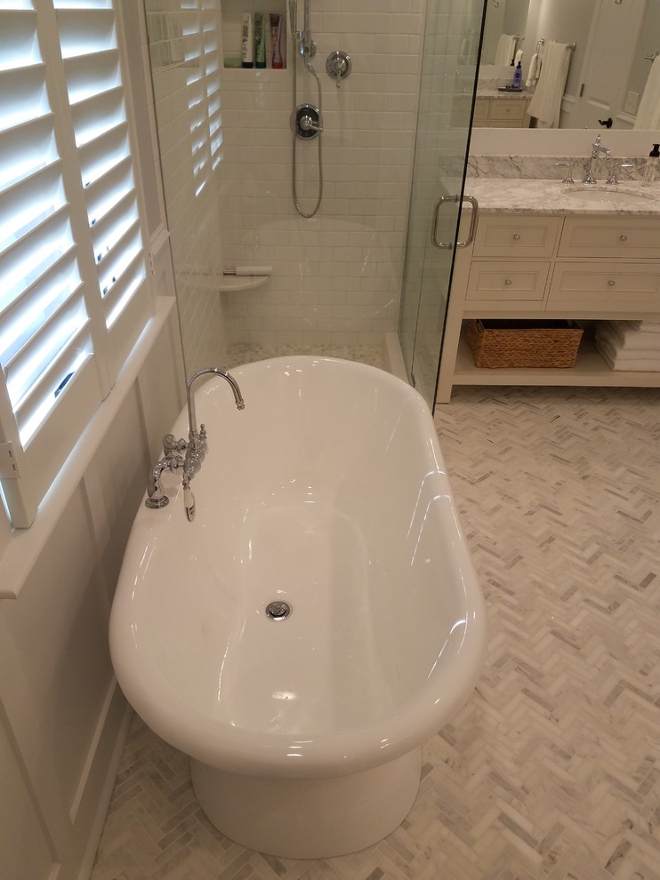 Klassisk inredning av ett mellanstort en-suite badrum, med möbel-liknande, vita skåp, ett fristående badkar, en hörndusch, en toalettstol med separat cisternkåpa, vit kakel, tunnelbanekakel, grå väggar, marmorgolv, ett undermonterad handfat, marmorbänkskiva, grått golv och dusch med gångjärnsdörr