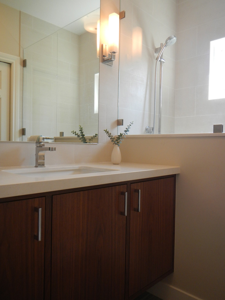 Foto på ett mellanstort funkis badrum med dusch, med ett undermonterad handfat, släta luckor, skåp i mellenmörkt trä, bänkskiva i kvarts, en toalettstol med hel cisternkåpa, vit kakel, keramikplattor, vita väggar och klinkergolv i keramik