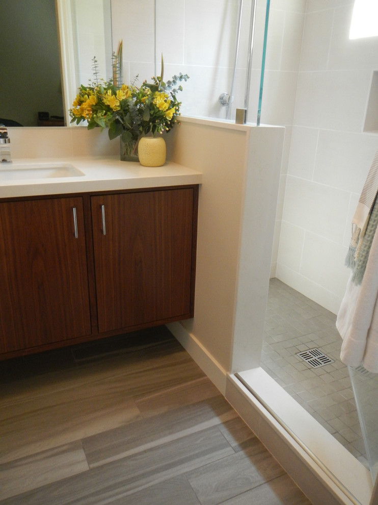 Modern inredning av ett mellanstort badrum med dusch, med ett undermonterad handfat, släta luckor, skåp i mellenmörkt trä, bänkskiva i kvarts, en toalettstol med hel cisternkåpa, vit kakel, keramikplattor, vita väggar och klinkergolv i keramik