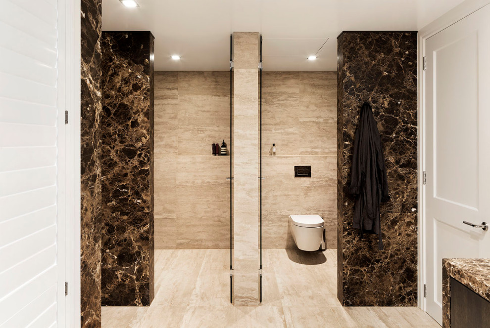 Design ideas for a large contemporary ensuite bathroom in Auckland with brown cabinets, a freestanding bath, a walk-in shower, a wall mounted toilet, brown tiles, marble tiles, beige walls, ceramic flooring, a built-in sink, marble worktops, beige floors, a hinged door, brown worktops, an enclosed toilet, double sinks and a built in vanity unit.