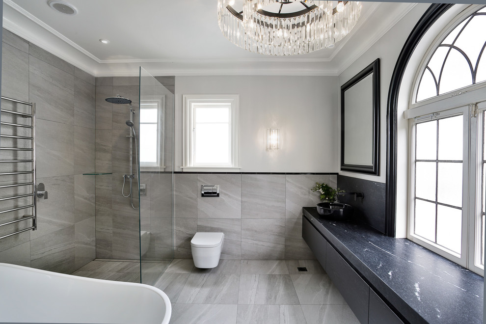 Cette photo montre une salle de bain principale tendance avec des portes de placard noires, une baignoire indépendante, une douche à l'italienne, WC suspendus, un mur gris et aucune cabine.